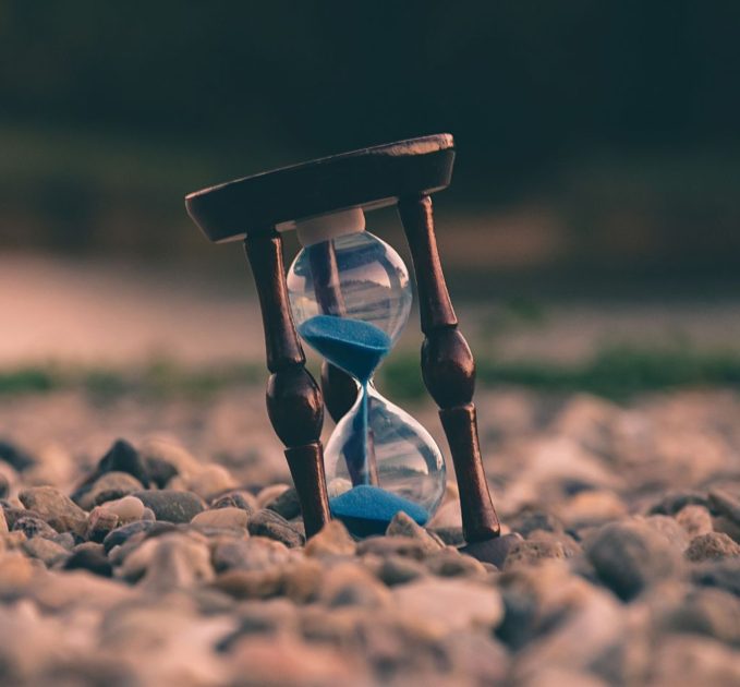 Hourglass with blue sand standing on rocks